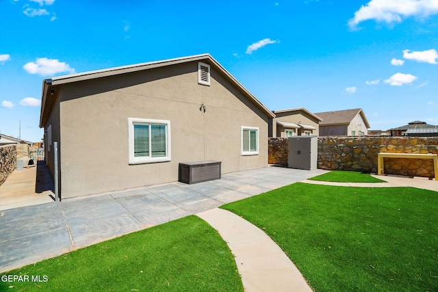 rear view of house with stucco siding, a lawn, a patio, and fence