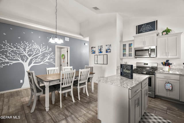 kitchen featuring light stone countertops, visible vents, wood tiled floor, stainless steel appliances, and a center island