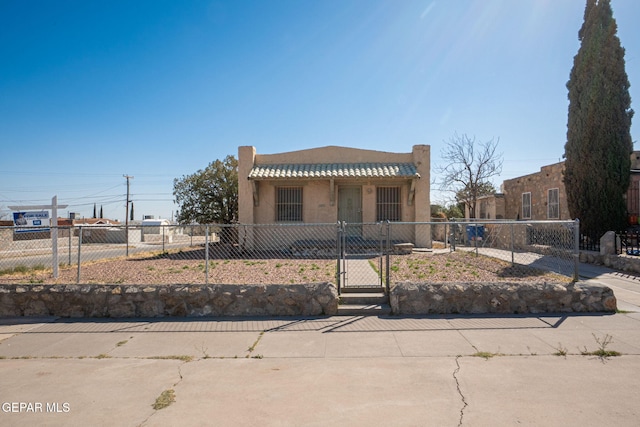 pueblo revival-style home featuring a gate, a fenced front yard, stucco siding, and a tile roof