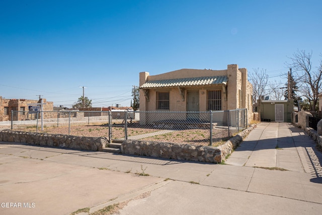 pueblo-style home with an outbuilding, stucco siding, concrete driveway, a fenced front yard, and a tiled roof