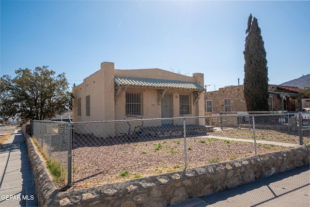 pueblo-style house with stucco siding, fence private yard, and a tiled roof