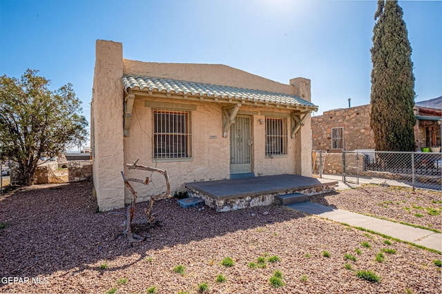 adobe home with a tiled roof, stucco siding, and fence