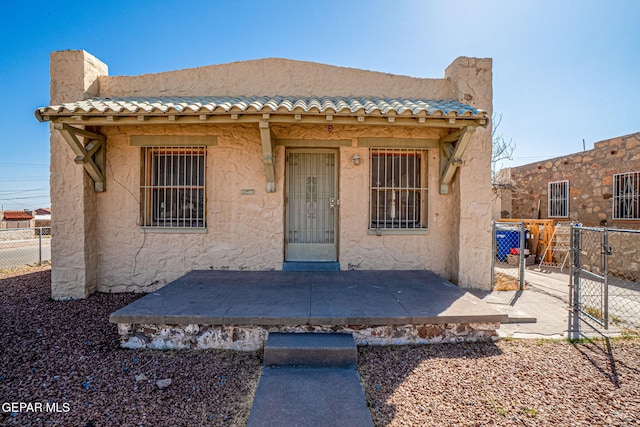 view of front of home featuring a tiled roof, a gate, fence, and stucco siding