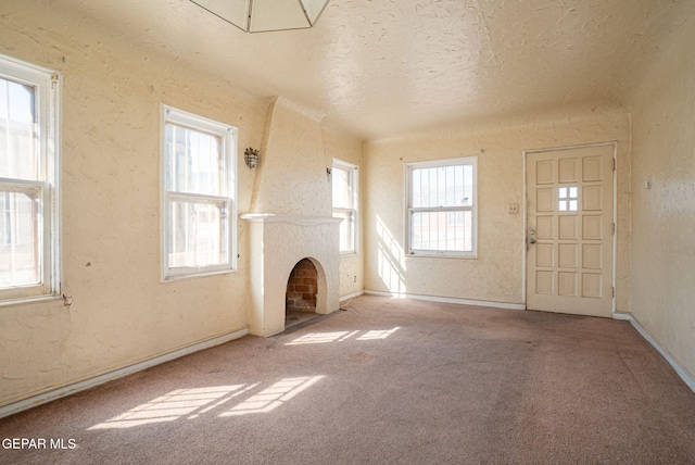 unfurnished living room featuring a fireplace with flush hearth, carpet, a textured wall, and a textured ceiling