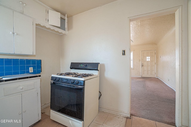 kitchen featuring light carpet, white gas stove, backsplash, tile countertops, and white cabinets