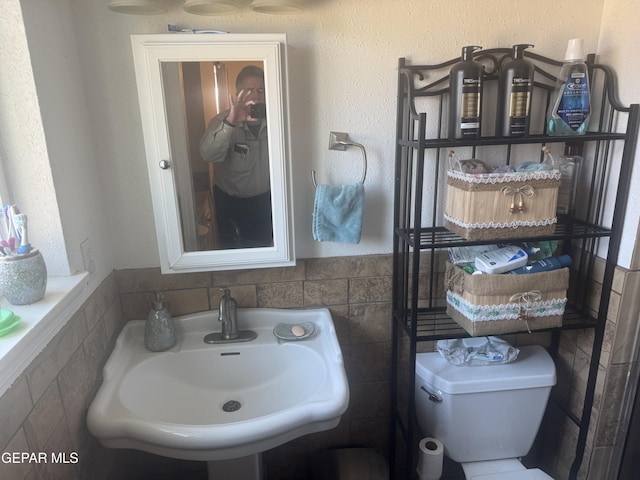 bathroom with toilet, tile walls, and a sink