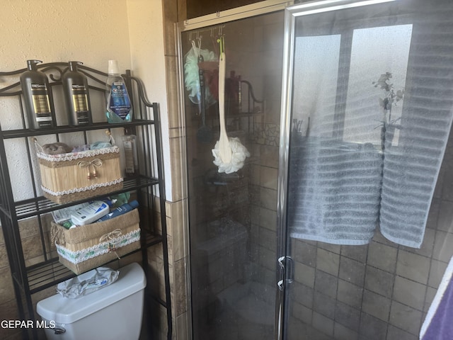 bathroom with a shower stall, toilet, and a textured wall