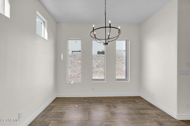 unfurnished dining area featuring dark wood-style floors, baseboards, and an inviting chandelier