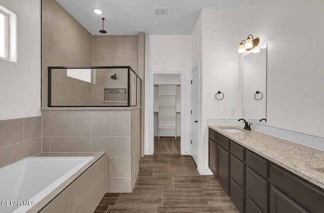 bathroom with visible vents, a stall shower, vanity, a bath, and a spacious closet