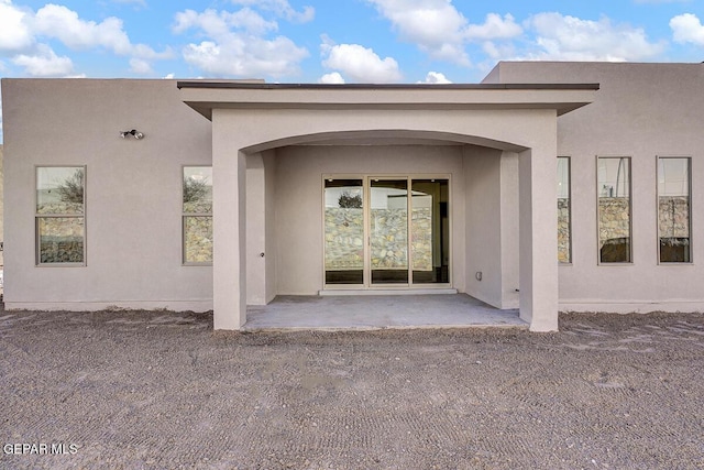 view of exterior entry featuring stucco siding and a patio area