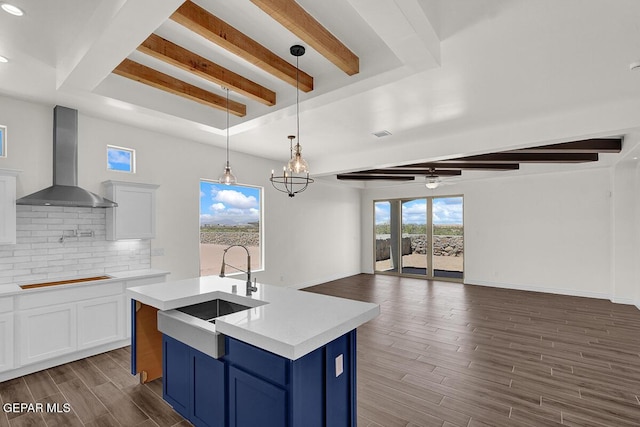 kitchen with backsplash, blue cabinetry, wall chimney range hood, light countertops, and a sink