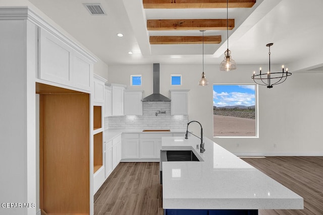 kitchen with visible vents, a kitchen island with sink, a sink, decorative backsplash, and wall chimney range hood