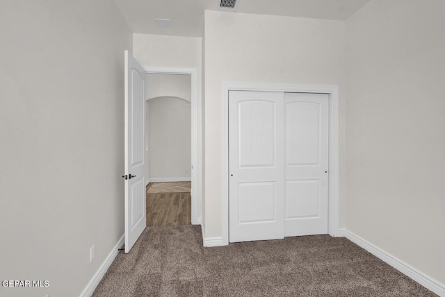 unfurnished bedroom featuring visible vents, carpet floors, baseboards, arched walkways, and a closet