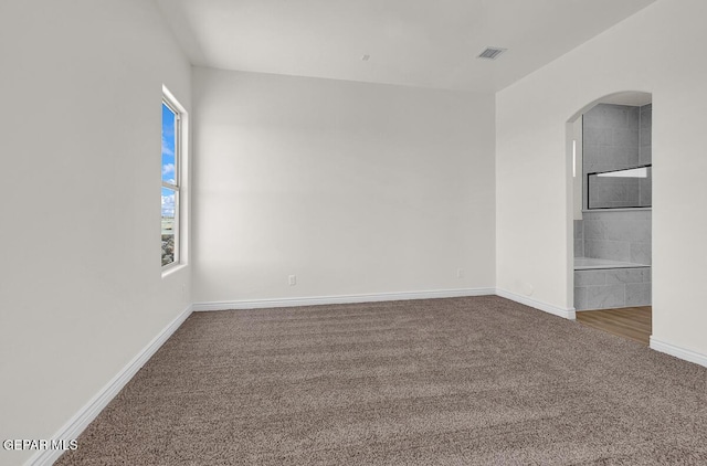 empty room featuring arched walkways, visible vents, baseboards, and carpet