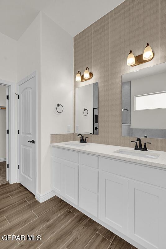 full bathroom with a sink, baseboards, wood finish floors, and double vanity