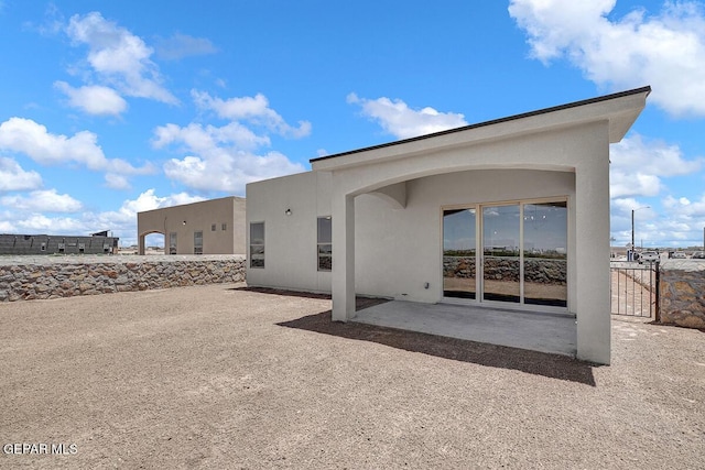 back of house featuring stucco siding, a patio, and a gate