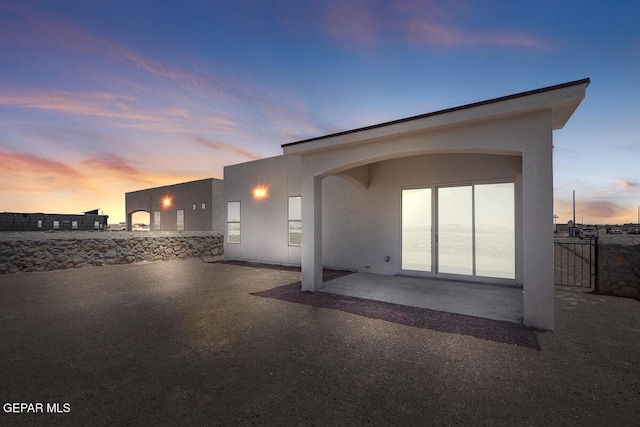 back of house at dusk featuring a patio, a gate, and stucco siding