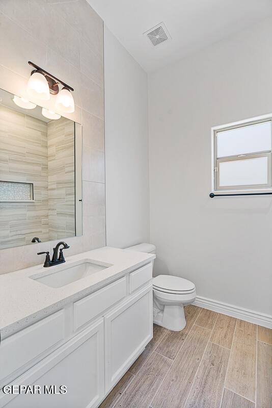 bathroom featuring vanity, baseboards, visible vents, wood tiled floor, and toilet