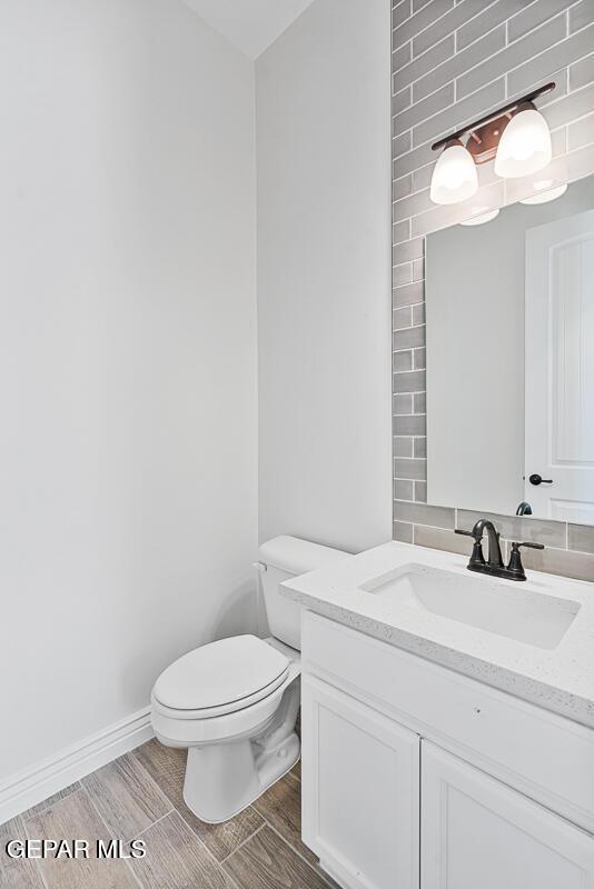 half bathroom with vanity, toilet, baseboards, and wood finish floors