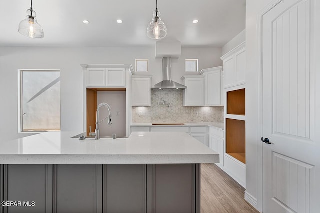 kitchen featuring light wood-type flooring, a center island with sink, backsplash, white cabinets, and wall chimney range hood