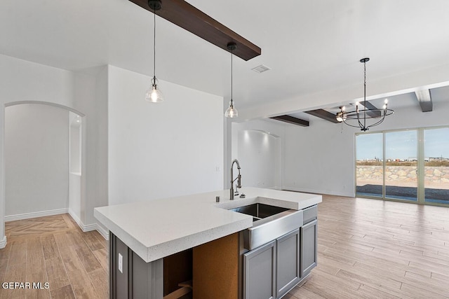 kitchen featuring arched walkways, light wood finished floors, light countertops, and a sink