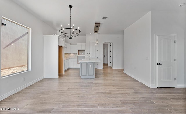 kitchen featuring tasteful backsplash, light countertops, light wood-style floors, arched walkways, and white cabinetry