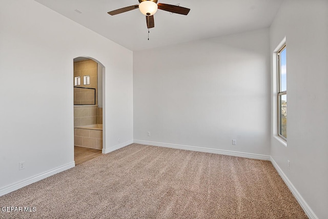 empty room with arched walkways, light colored carpet, baseboards, and ceiling fan