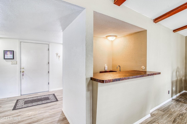 bar with wood finished floors, baseboards, beam ceiling, indoor wet bar, and a textured ceiling