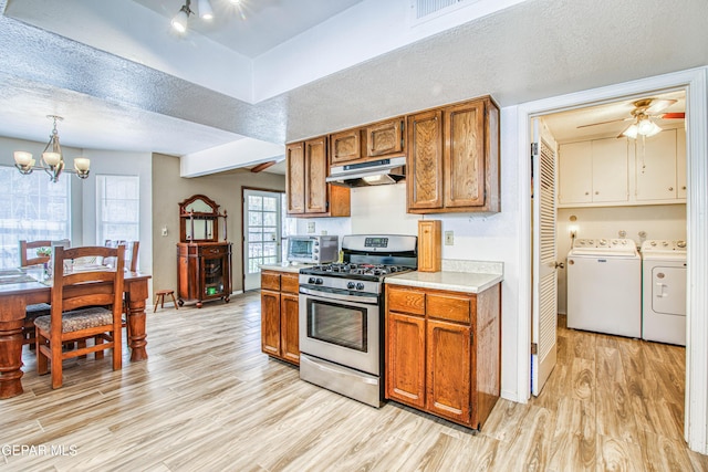 kitchen with light wood-style flooring, light countertops, under cabinet range hood, stainless steel gas range oven, and independent washer and dryer