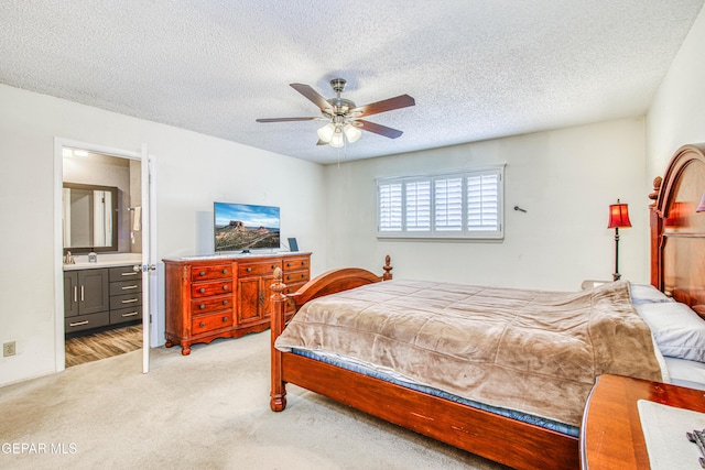 bedroom with a textured ceiling, a ceiling fan, light colored carpet, and connected bathroom