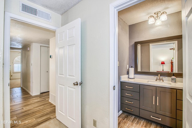 bathroom with vanity, wood finished floors, baseboards, visible vents, and a textured ceiling