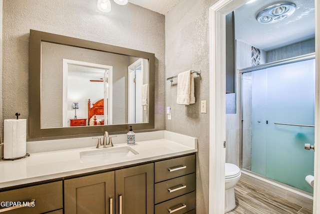 full bath with vanity, toilet, a shower stall, and a textured wall