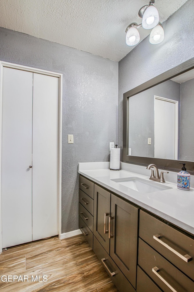 bathroom with a textured ceiling, wood finished floors, vanity, and a textured wall