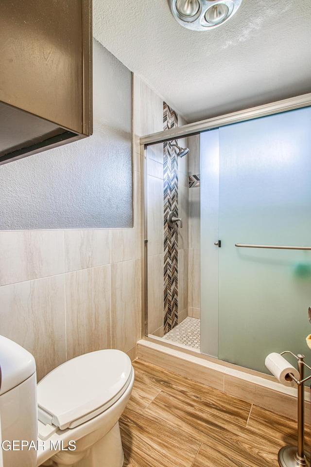 bathroom featuring a stall shower, toilet, tile walls, and a textured ceiling