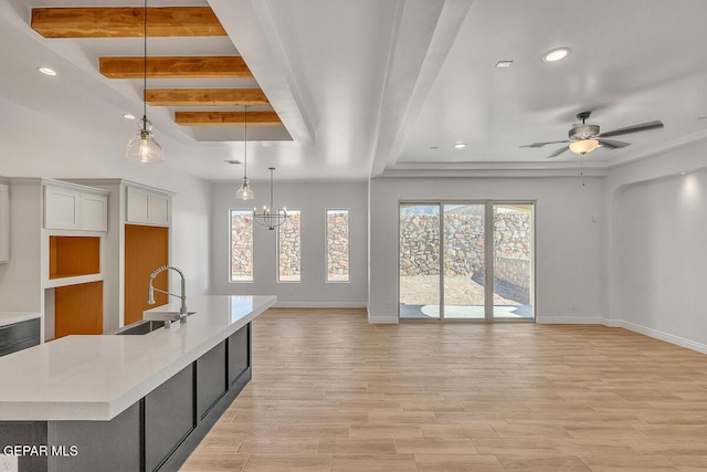 kitchen featuring beam ceiling, light wood-style flooring, a sink, open floor plan, and light countertops