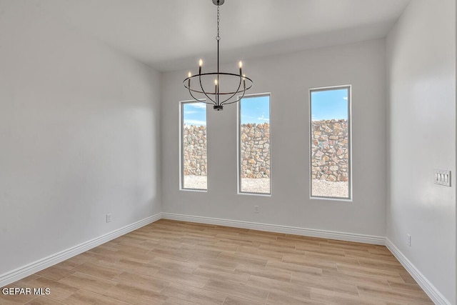 unfurnished room featuring baseboards, light wood-type flooring, and a chandelier