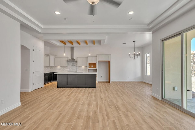 kitchen with light wood-style flooring, white cabinets, wall chimney range hood, decorative backsplash, and light countertops