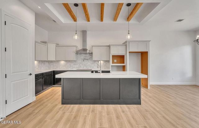 kitchen with decorative backsplash, wall chimney range hood, light wood finished floors, and a sink