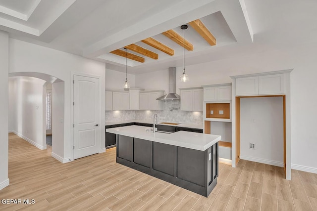 kitchen featuring wood finish floors, arched walkways, decorative backsplash, white cabinets, and wall chimney range hood