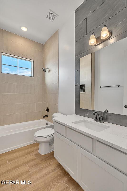 bathroom with vanity, wood finished floors, visible vents, tub / shower combination, and toilet