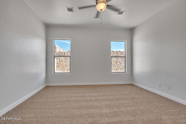 carpeted spare room with visible vents, baseboards, and a ceiling fan