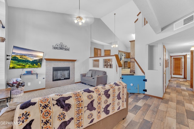 living area featuring wood finished floors, baseboards, visible vents, high vaulted ceiling, and a tile fireplace