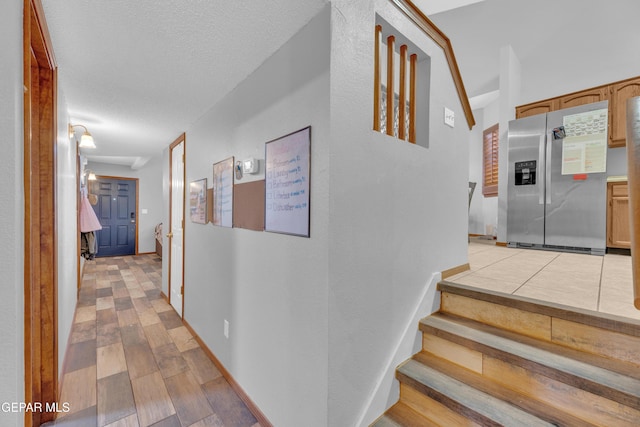 hall featuring stairs, baseboards, light wood finished floors, and a textured ceiling