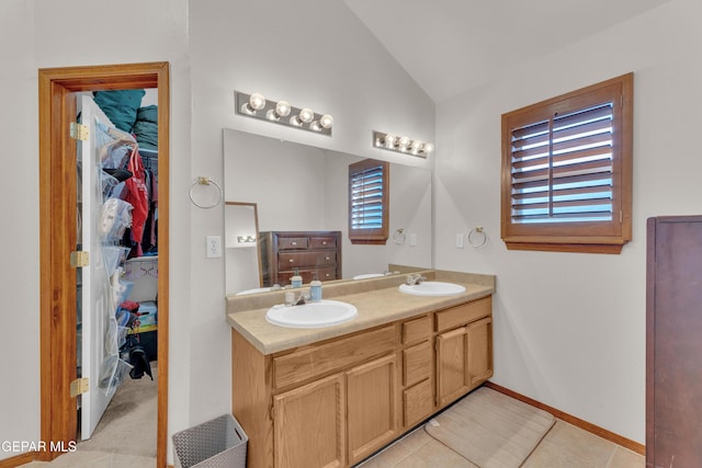 full bath with double vanity, vaulted ceiling, a walk in closet, and a sink