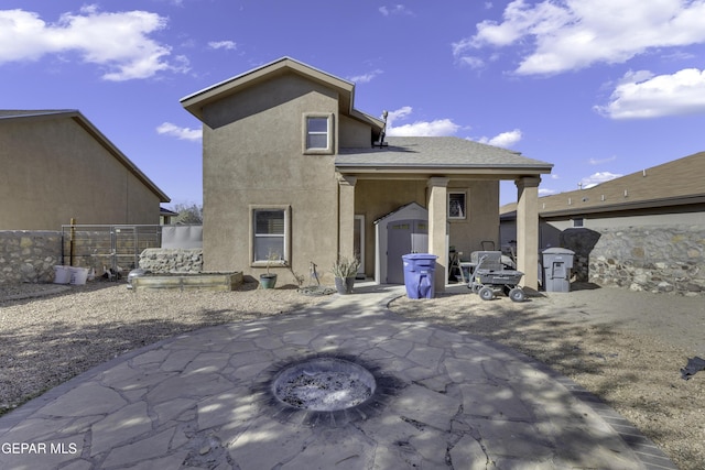 rear view of house with fence, stucco siding, a storage shed, an outdoor structure, and a patio area