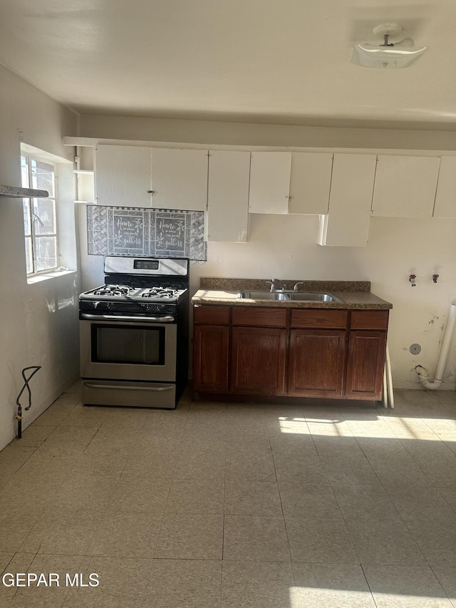 kitchen with dark countertops, white cabinetry, stainless steel gas range, and a sink