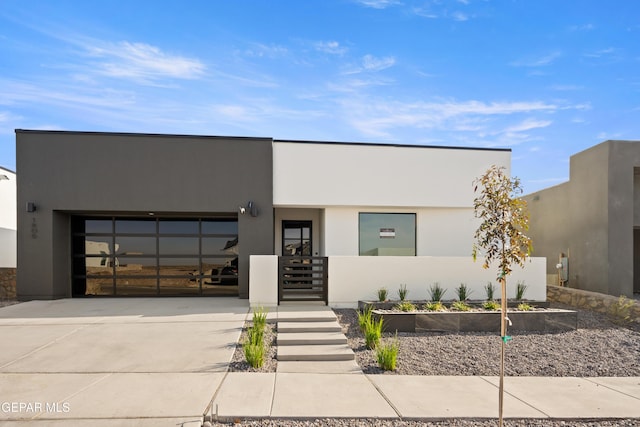 contemporary home featuring a vegetable garden, a garage, driveway, and stucco siding