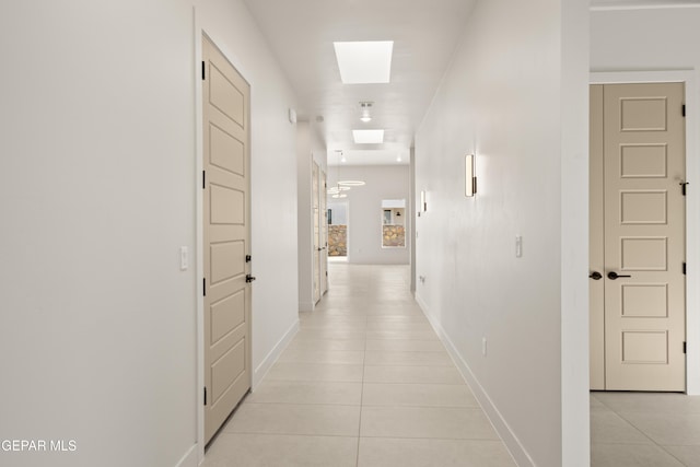 corridor featuring a skylight, baseboards, and light tile patterned flooring