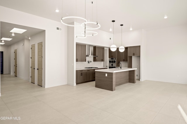 kitchen featuring modern cabinets, gas cooktop, wall chimney exhaust hood, light countertops, and decorative backsplash