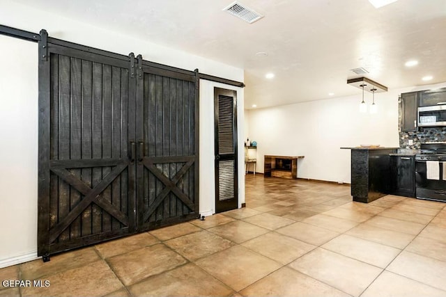 kitchen featuring visible vents, decorative backsplash, black range with gas stovetop, a barn door, and stainless steel microwave